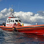Load image into Gallery viewer, Red and white SAR boat on the water with a blue sky and clouds in the background.
